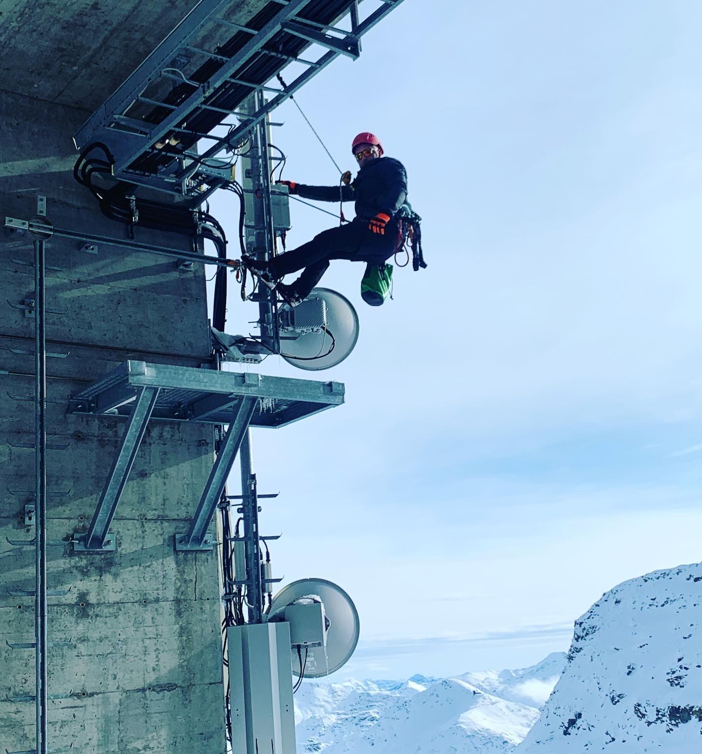 A person working beside dish antennas on a mast in a snowy setting.