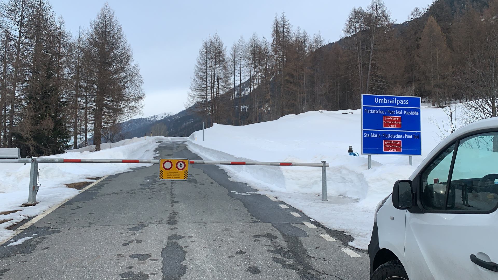 A road and work vehicle beside snow-covered mountain slopes.