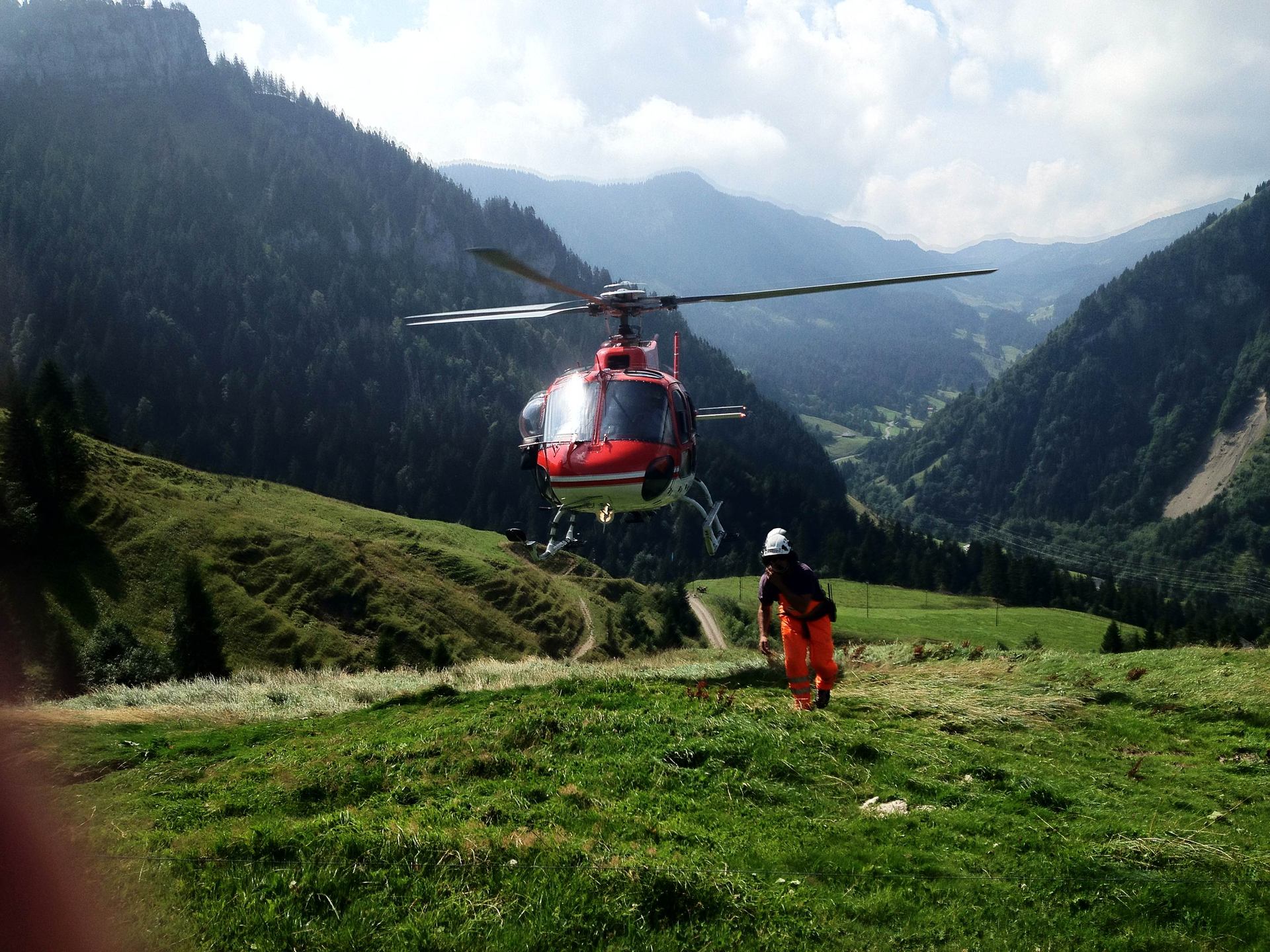 A red helicopter above a grassy mountain clearing.