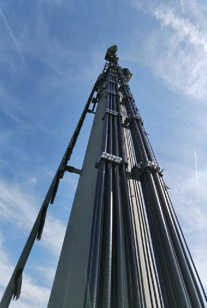 A close upward view of a mast, brackets and cables.