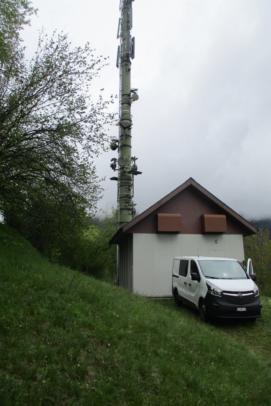 A telecommunications mast beside a small building and work vehicle.