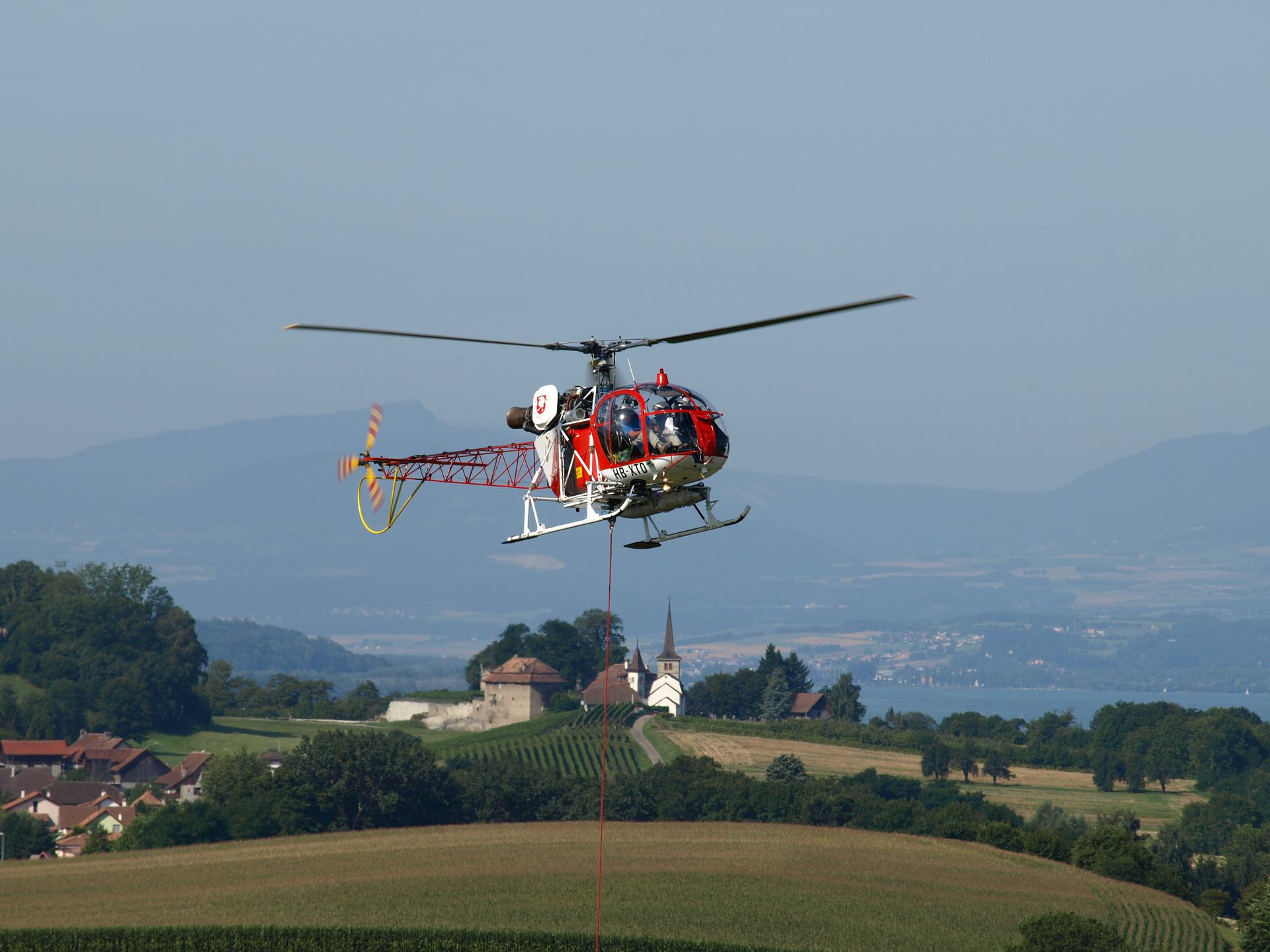 A red helicopter carrying a suspended load above the landscape.