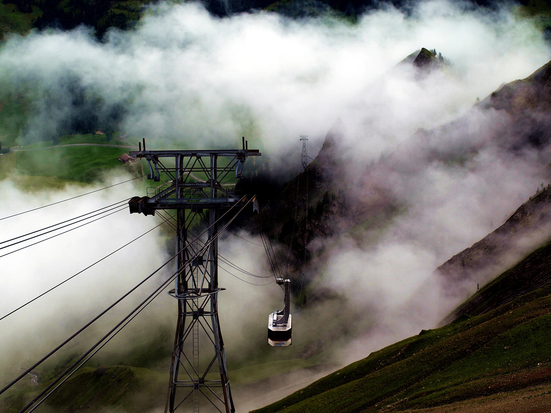A cableway tower and cabin amid clouds on a mountainside.