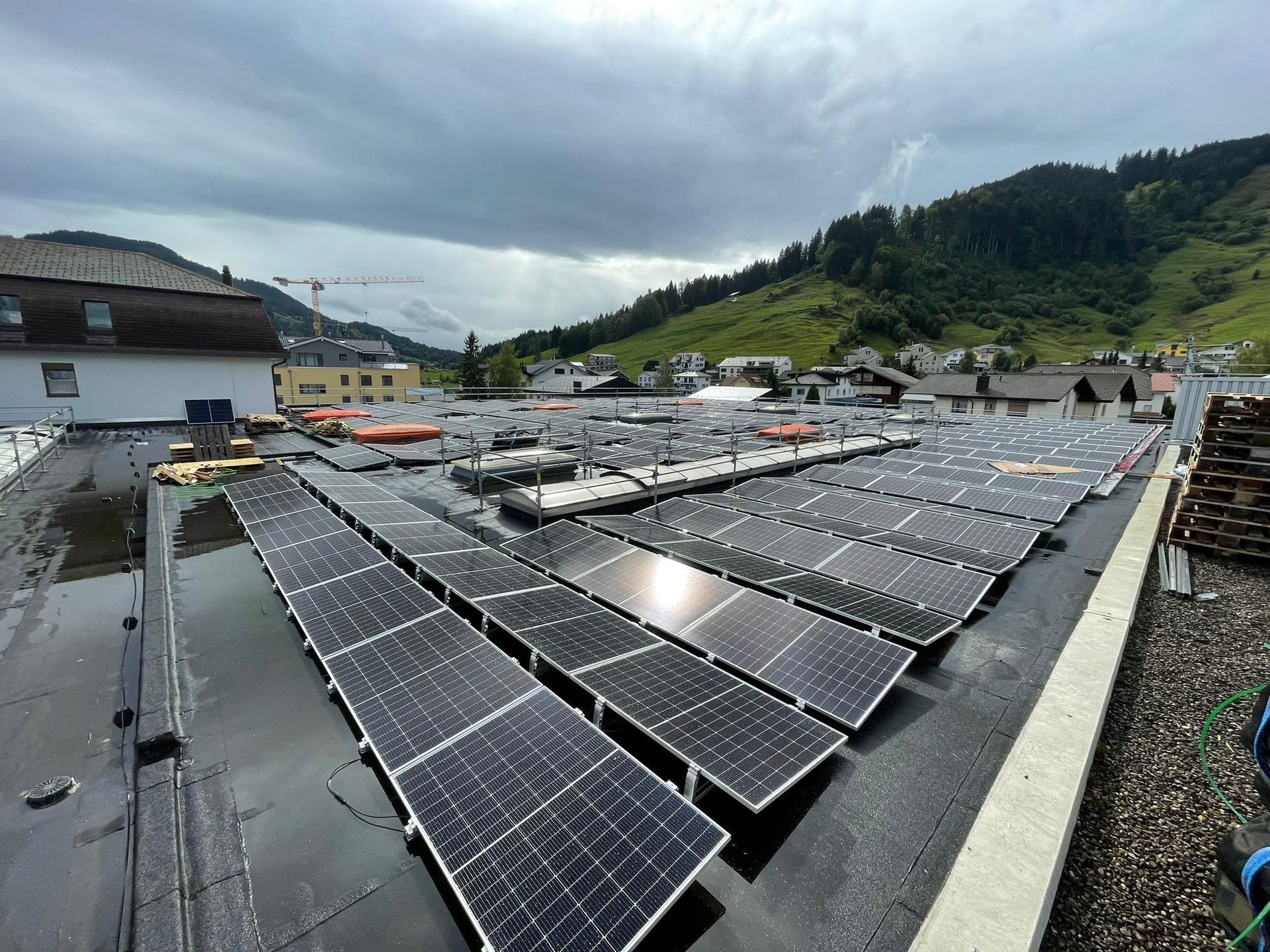 A rooftop solar array with buildings and green hills beyond.