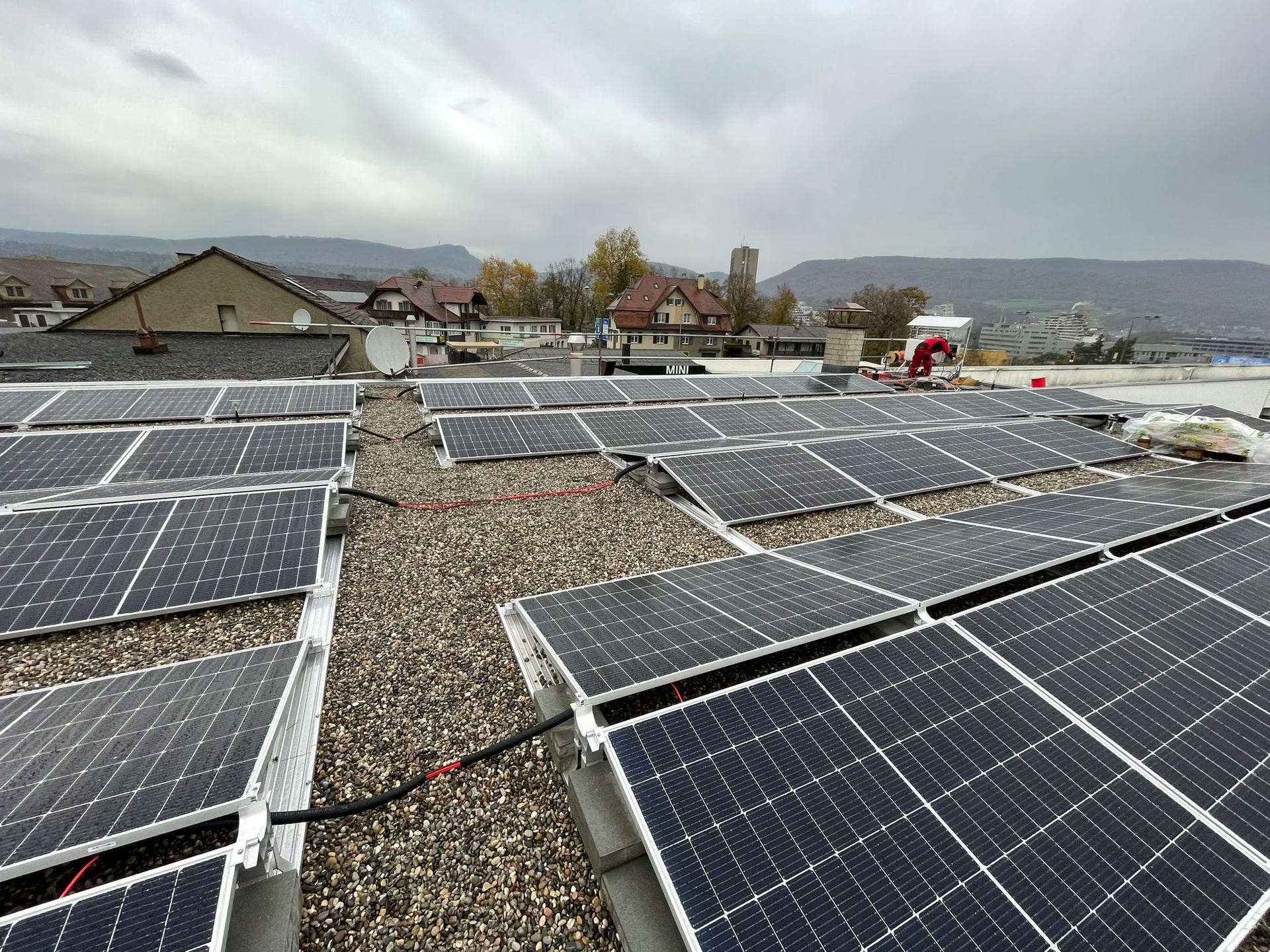 Groups of photovoltaic modules spaced across a gravel rooftop.